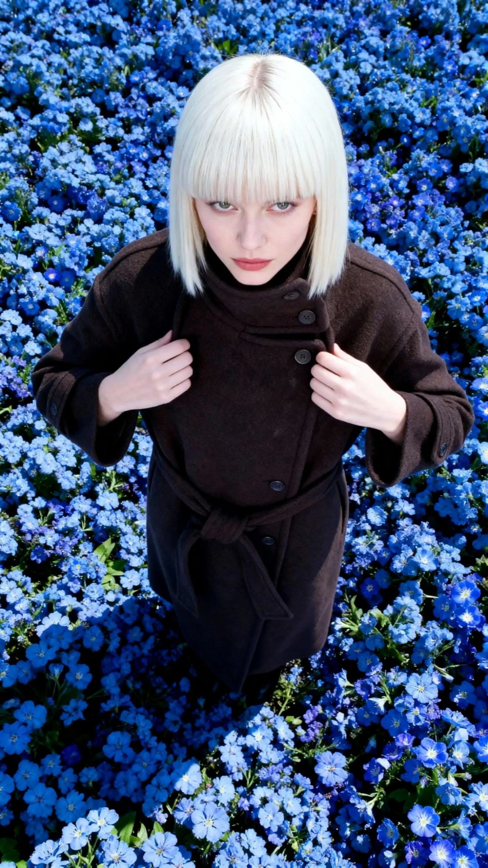 a woman with white hair sitting in a field of blue flowers