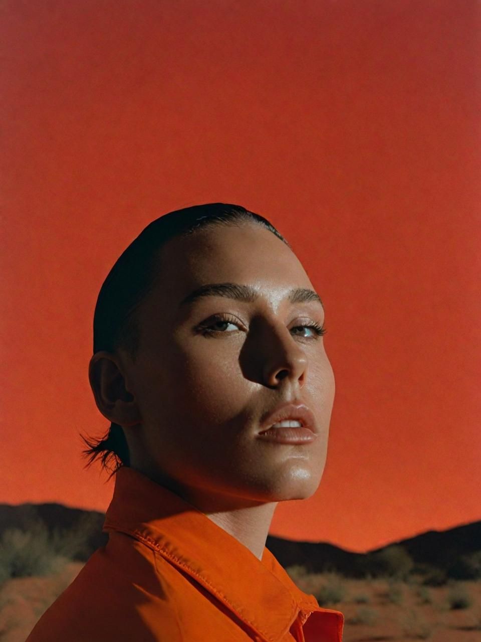 a woman standing in the desert with an orange sky in the background