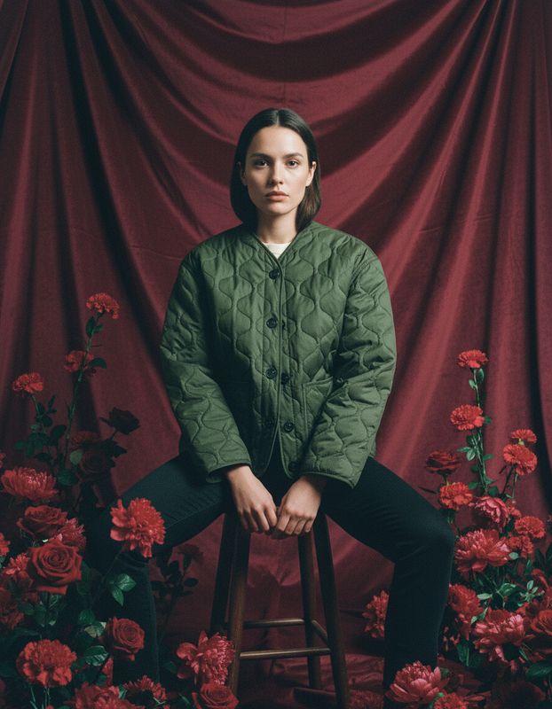 a woman sitting on a stool in front of red flowers