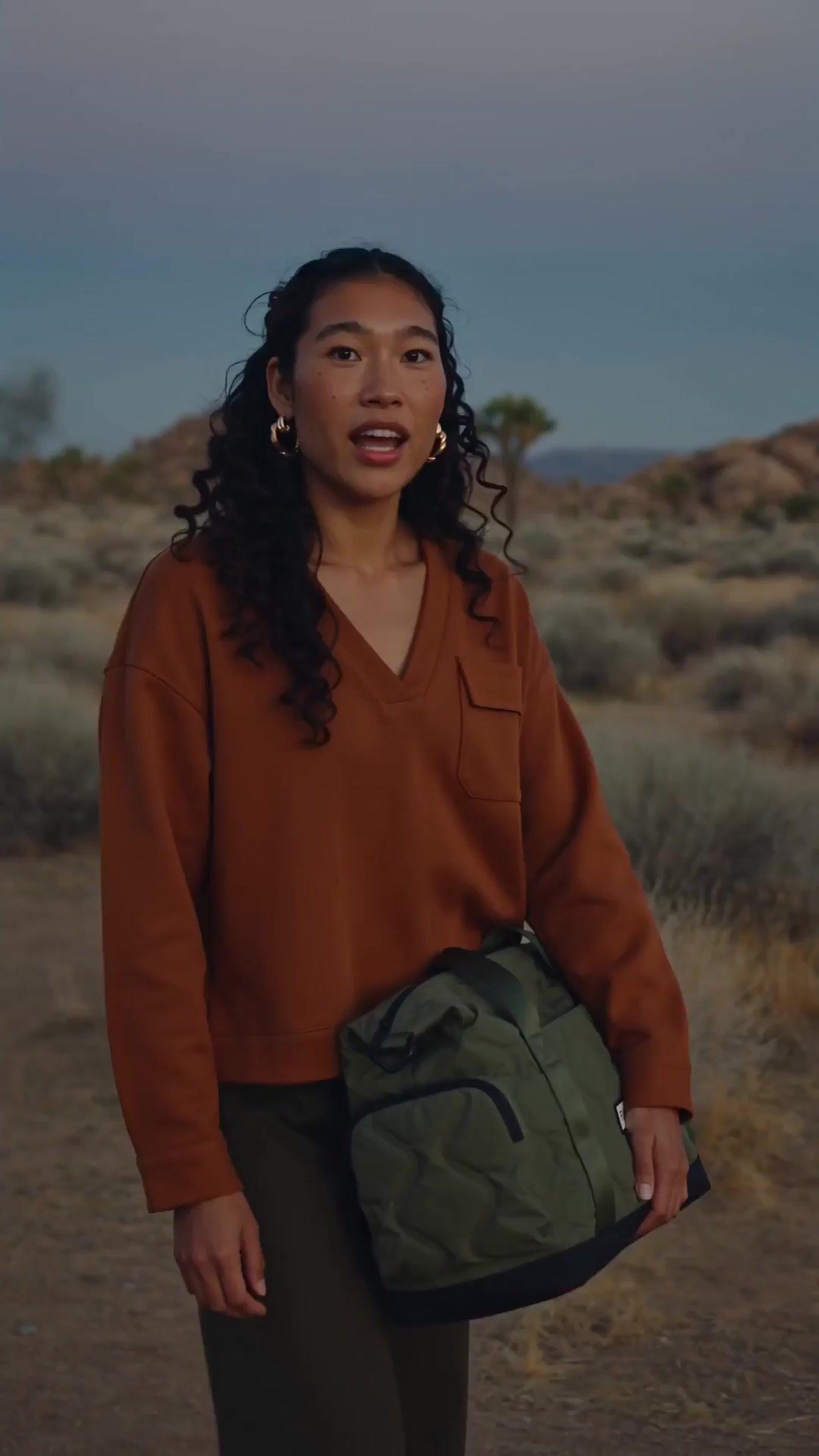 a woman in a brown sweater is holding a green bag