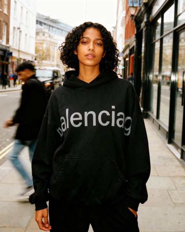 a woman standing on a sidewalk wearing a black hoodie