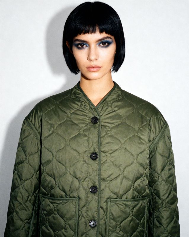 a woman with black hair wearing a green jacket