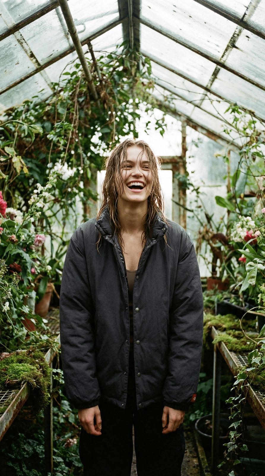 a man with long hair standing in a greenhouse