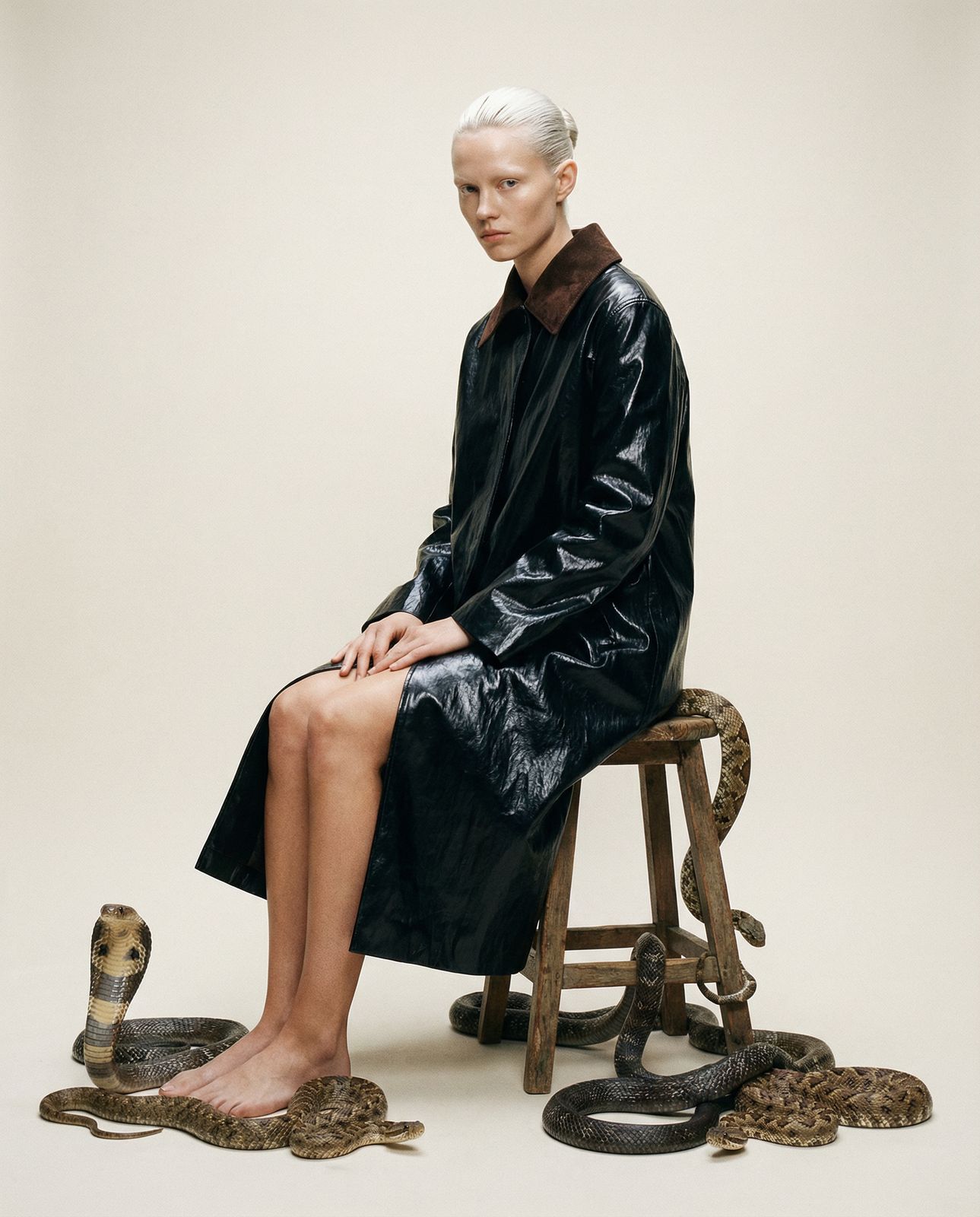 a woman sitting on top of a stool next to a snake