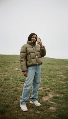 a woman standing in a field taking a picture with her cell phone