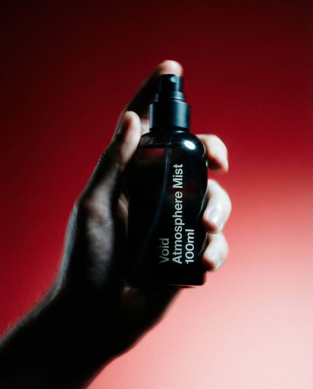 a hand holding a black bottle with a red background