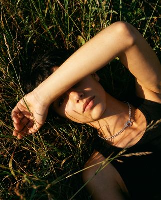 a woman laying in the grass wearing a necklace