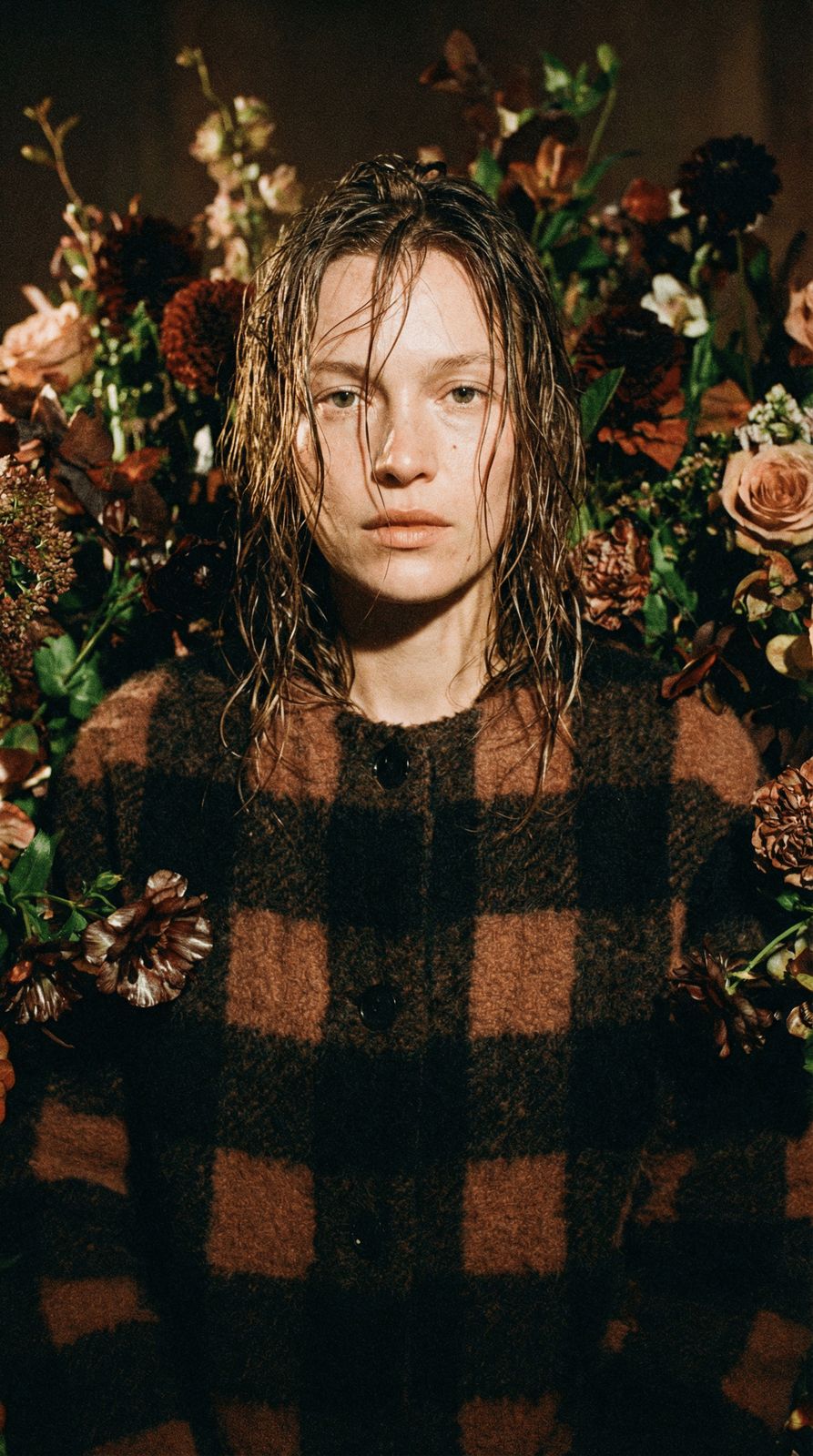 a man with long hair standing in front of flowers
