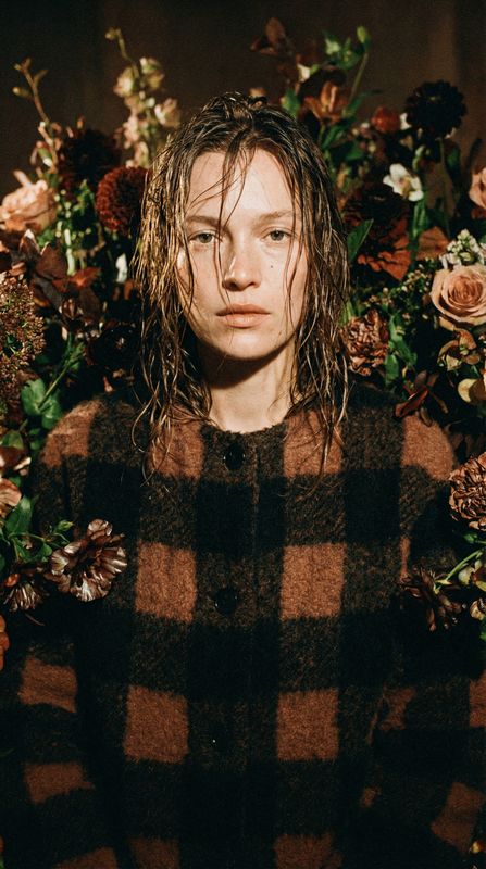 a man with long hair standing in front of flowers
