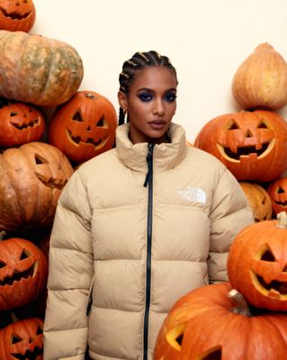 a woman standing in front of a pile of pumpkins