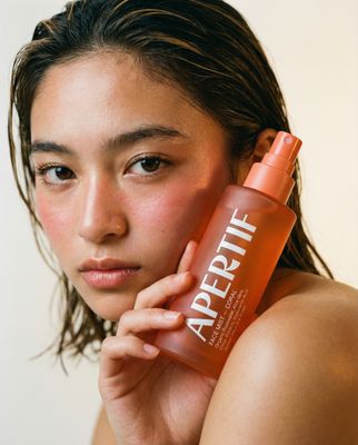 a woman holding a bottle of apricot next to her face
