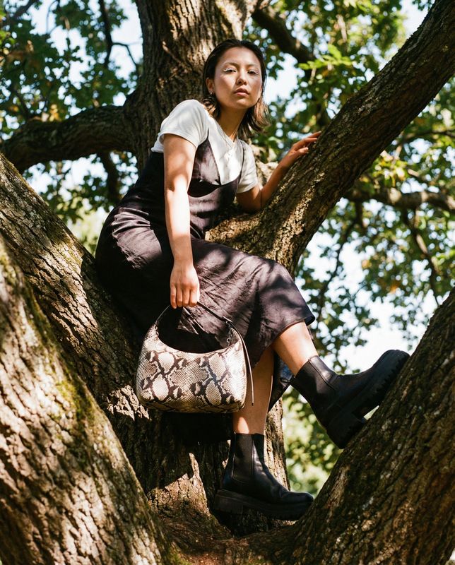 a woman sitting in a tree holding a purse