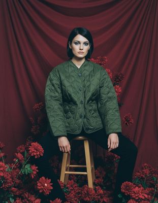 a woman sitting on a stool in front of red flowers