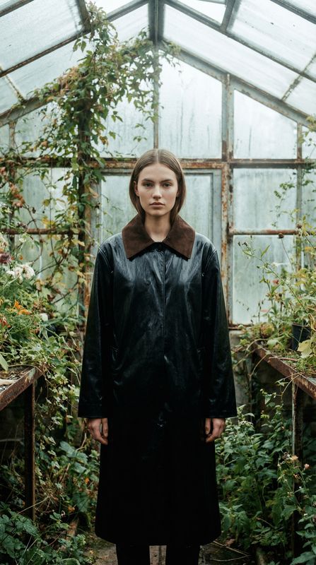 a woman standing in a greenhouse wearing a black coat
