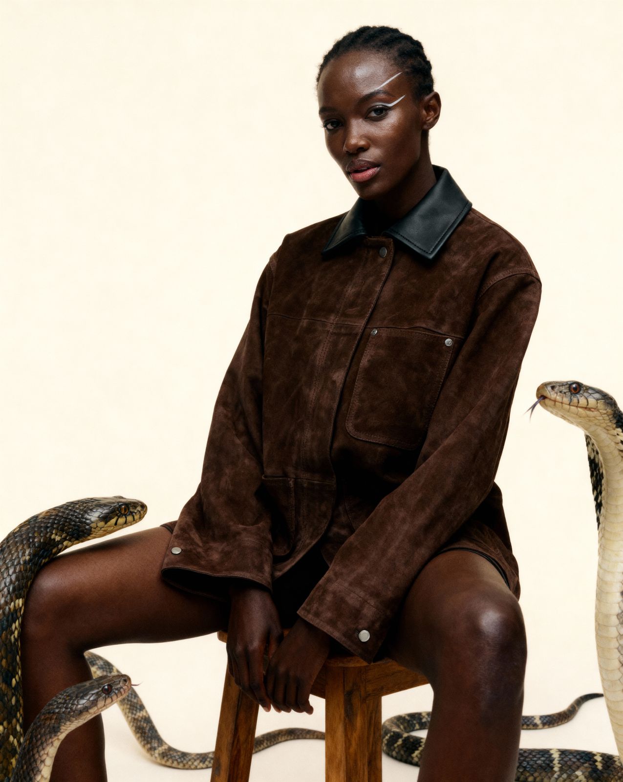 a woman sitting on a stool next to two snakes