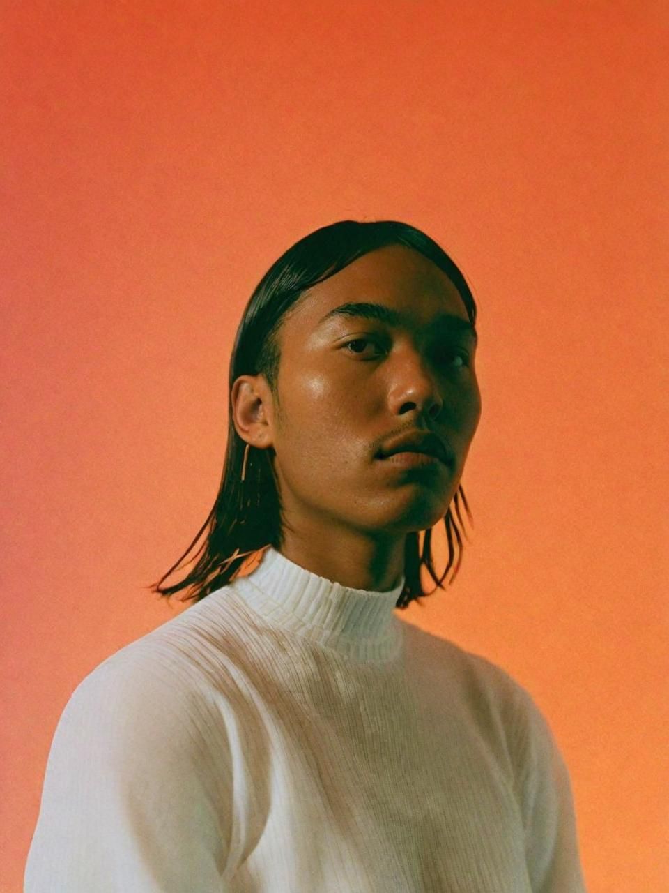 a man with long hair standing in front of an orange background