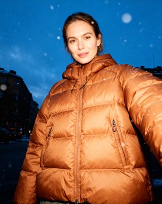 a woman standing in the snow wearing a brown jacket