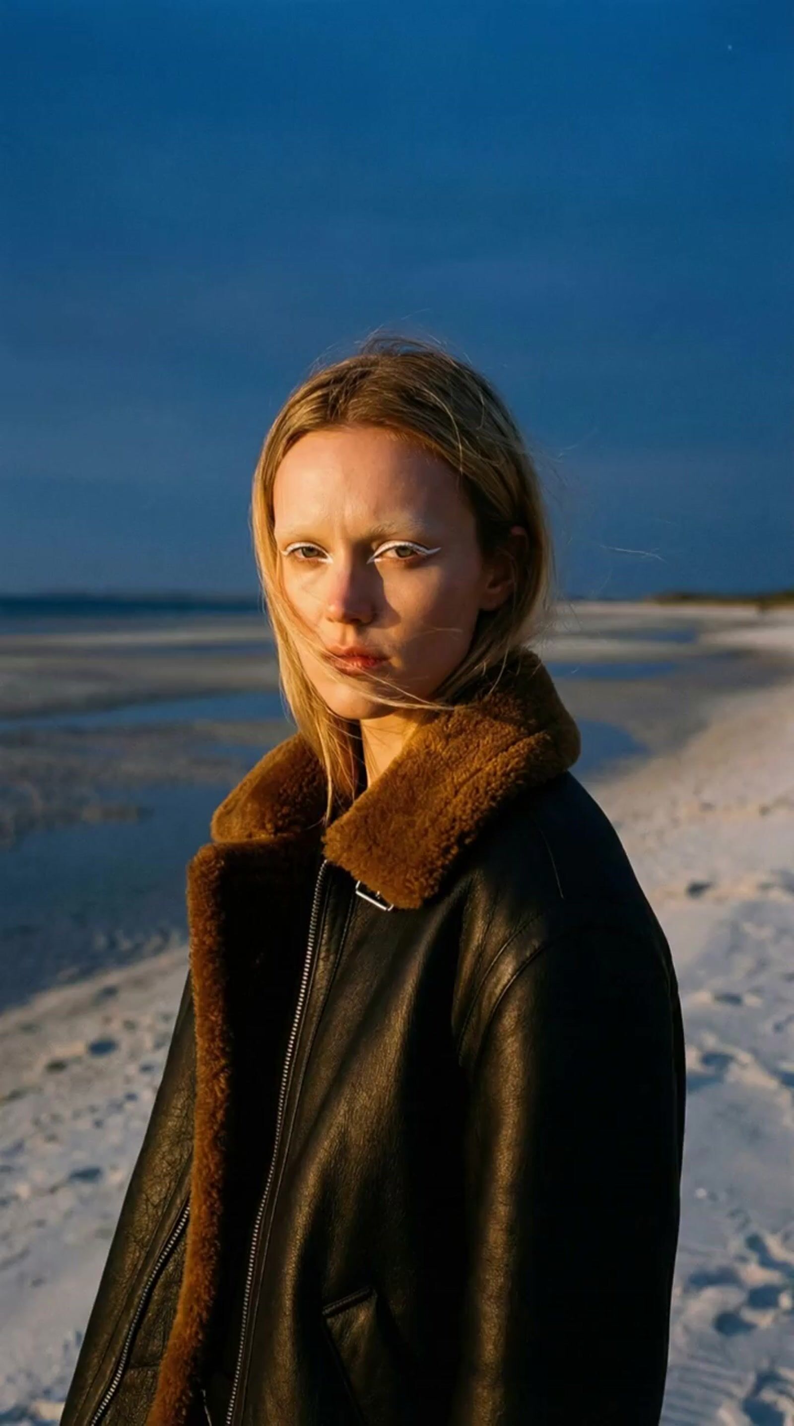 a woman in a leather jacket standing on a beach