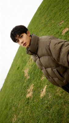 a young man in a puffy coat standing in a field