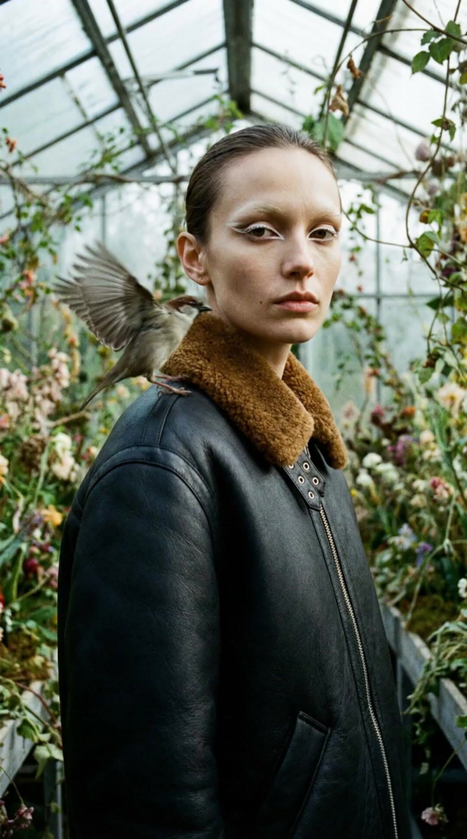 a woman standing in a greenhouse with a bird on her shoulder