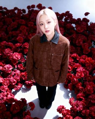 a woman with pink hair standing in a field of flowers