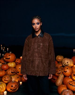 a woman standing in front of a pile of pumpkins
