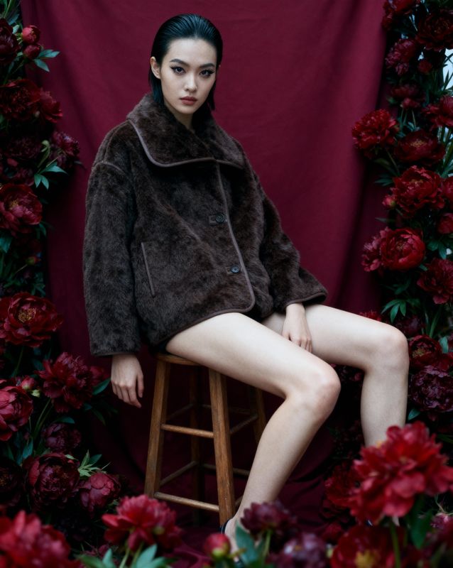 a woman in a fur coat sitting on a stool