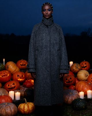 a woman standing in front of a pile of pumpkins