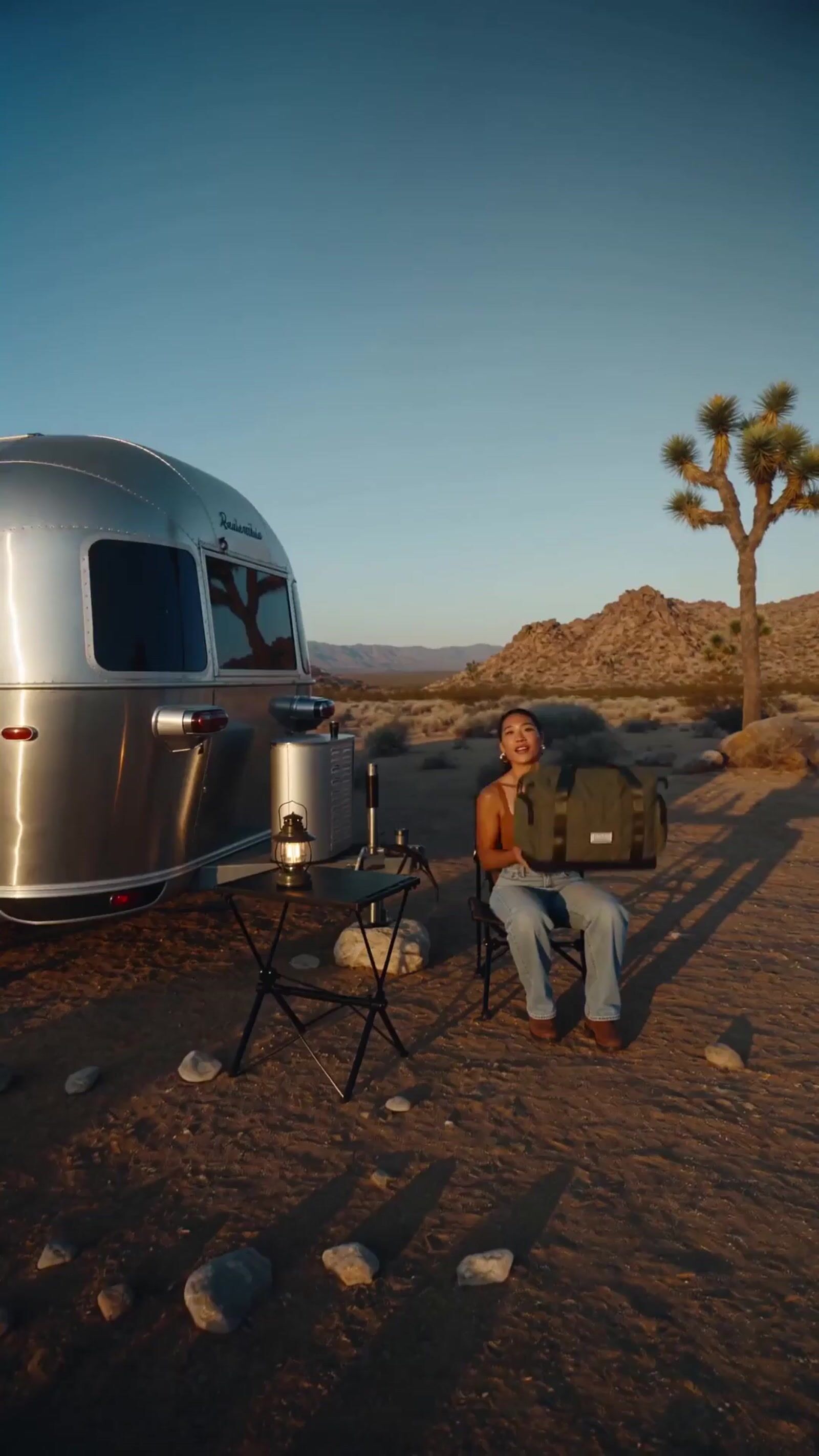 a man sitting in a chair next to a silver trailer