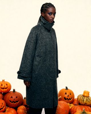 a woman standing in front of a pile of pumpkins