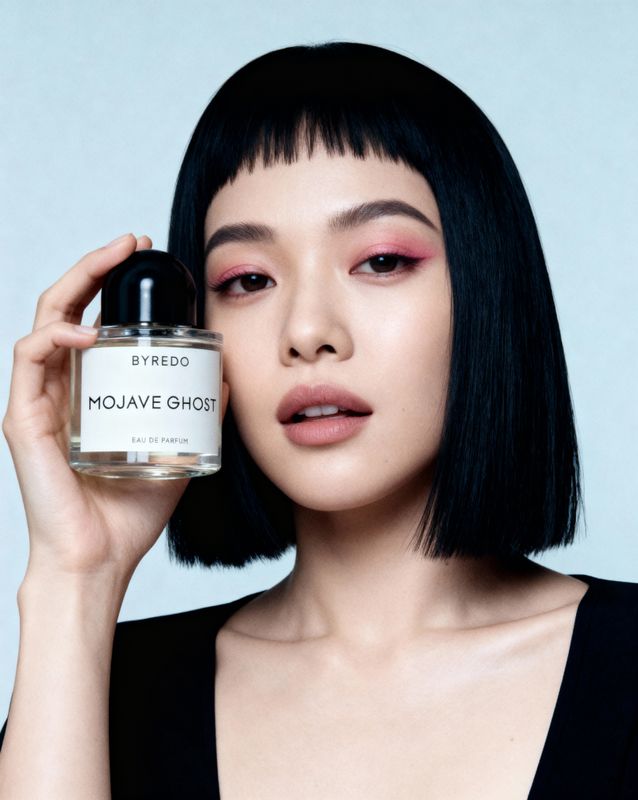 a woman holding a bottle of perfume in front of her face