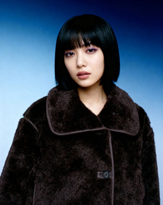 a woman with black hair wearing a brown coat
