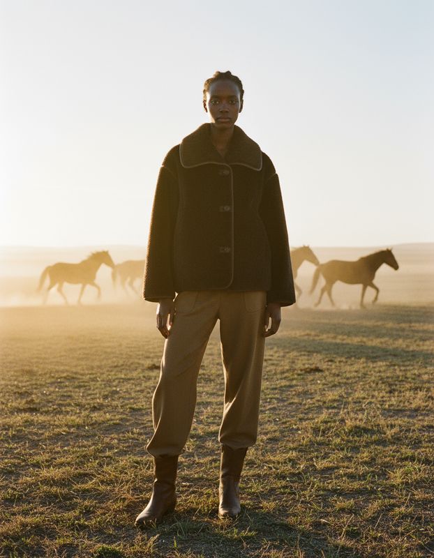 a man standing in a field with horses in the background