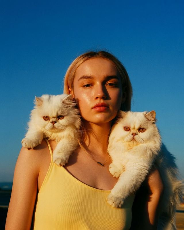 a woman in a yellow tank top holding two cats