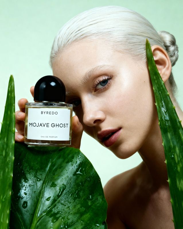 a woman holding a bottle of perfume next to a plant
