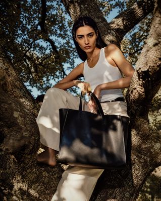 a woman sitting in a tree holding a black bag