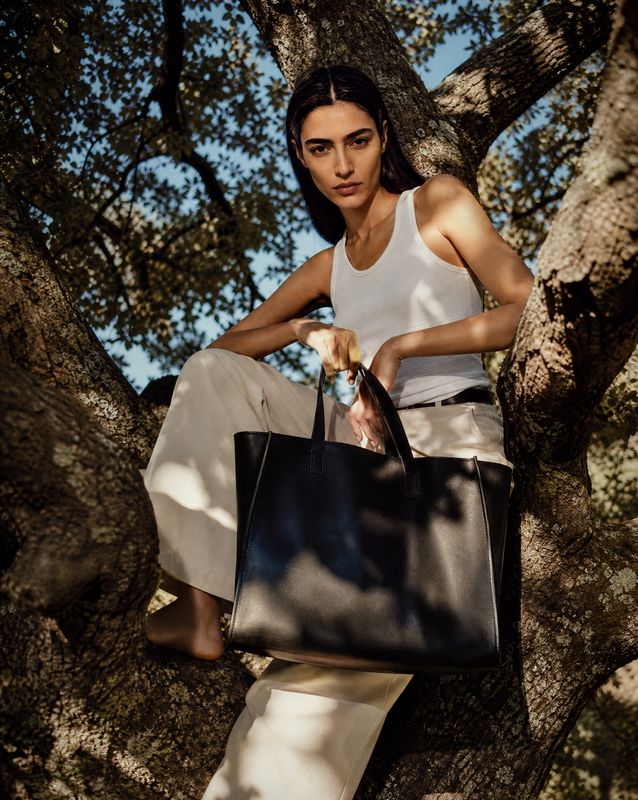 a woman sitting in a tree holding a black bag