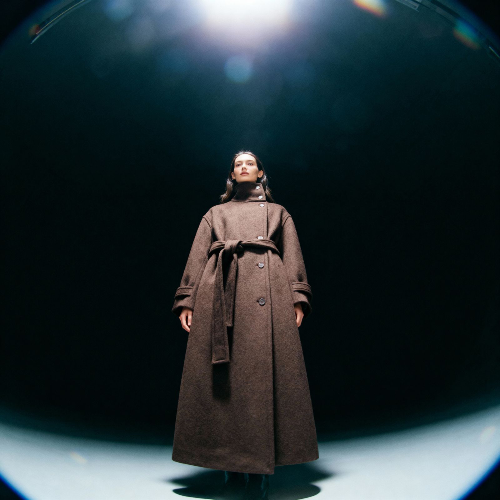 a woman in a brown coat standing in a dark room