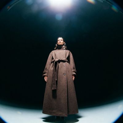 a woman in a brown coat standing in a dark room