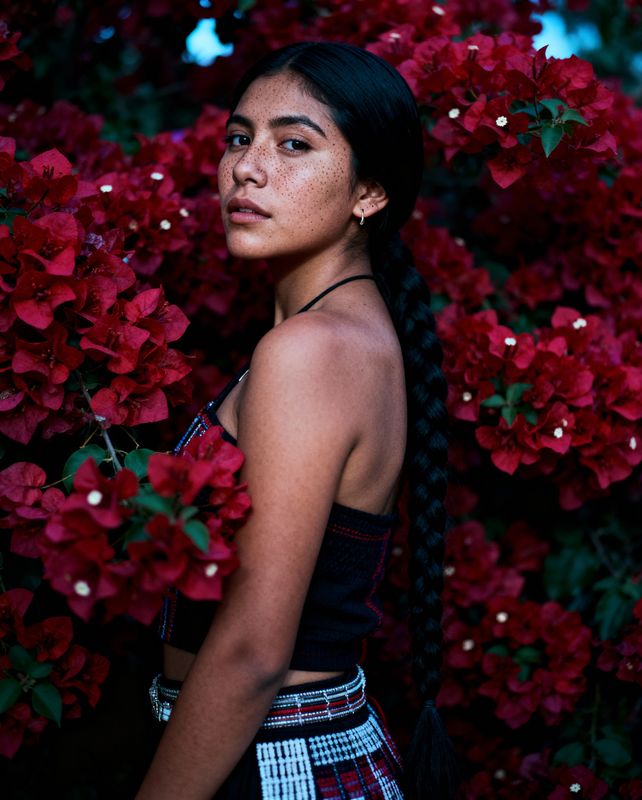 a woman standing in front of a bunch of red flowers