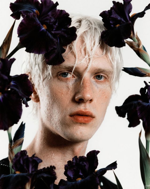 a man with white hair and blue eyes surrounded by flowers