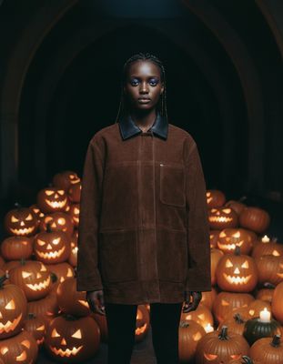 a woman standing in front of a pile of pumpkins