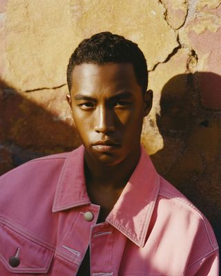 a man in a pink jacket standing in front of a wall
