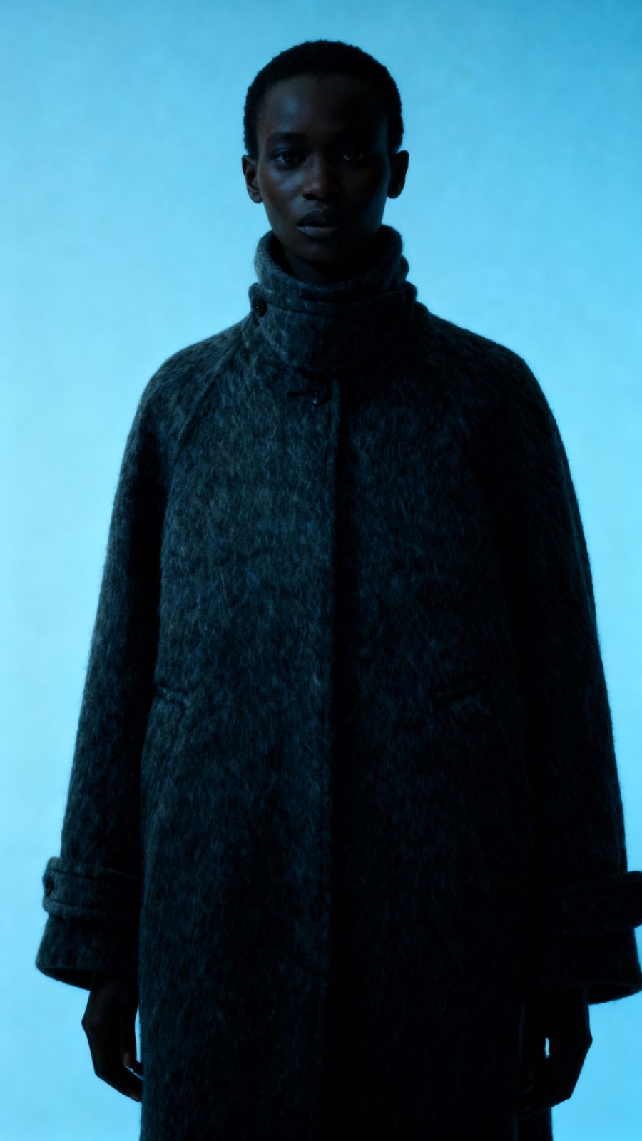 a man in a black coat standing in front of a blue background
