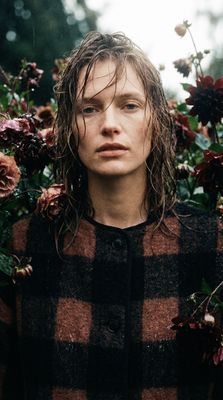 a man with long hair standing in front of flowers