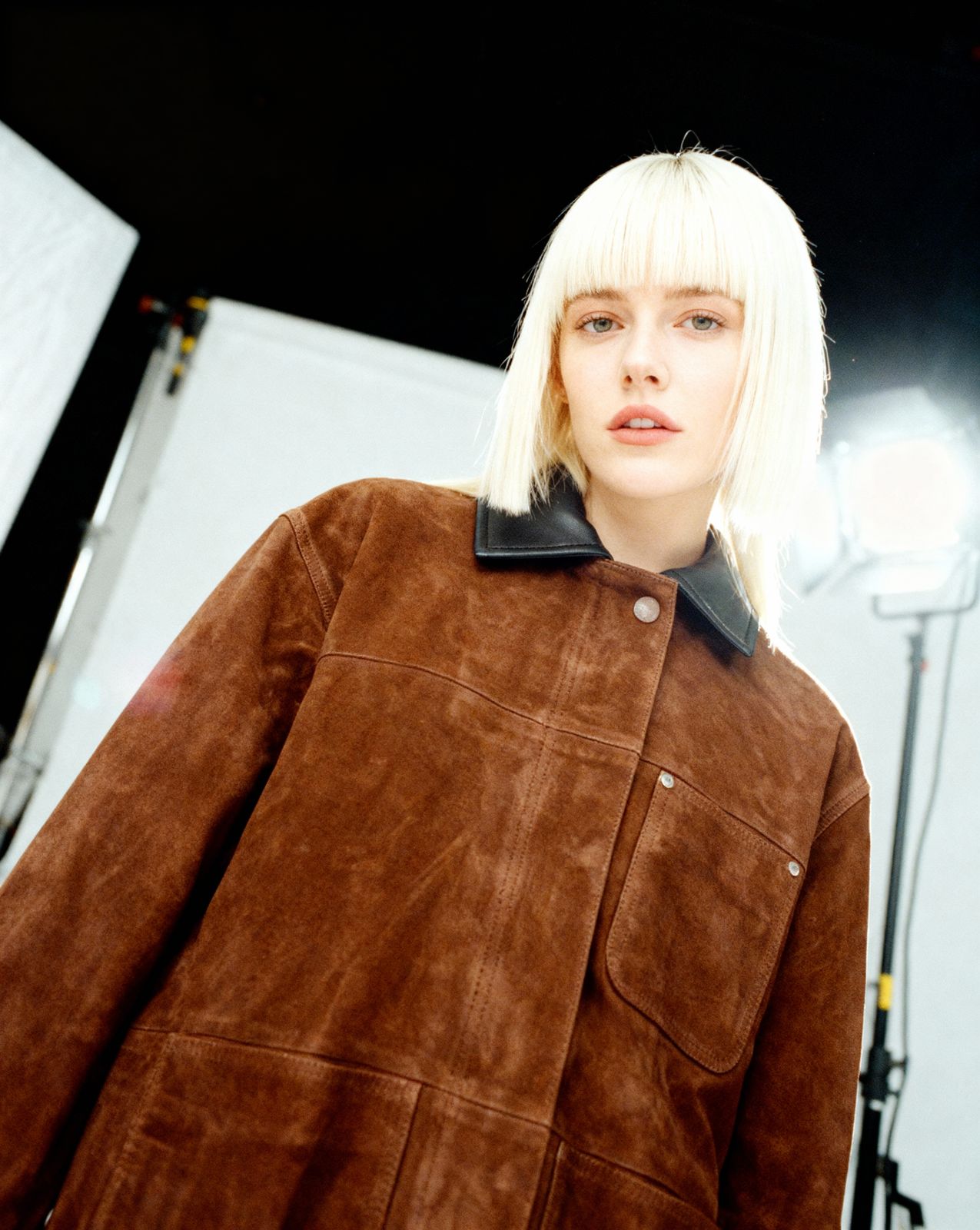 a woman with blonde hair wearing a brown jacket