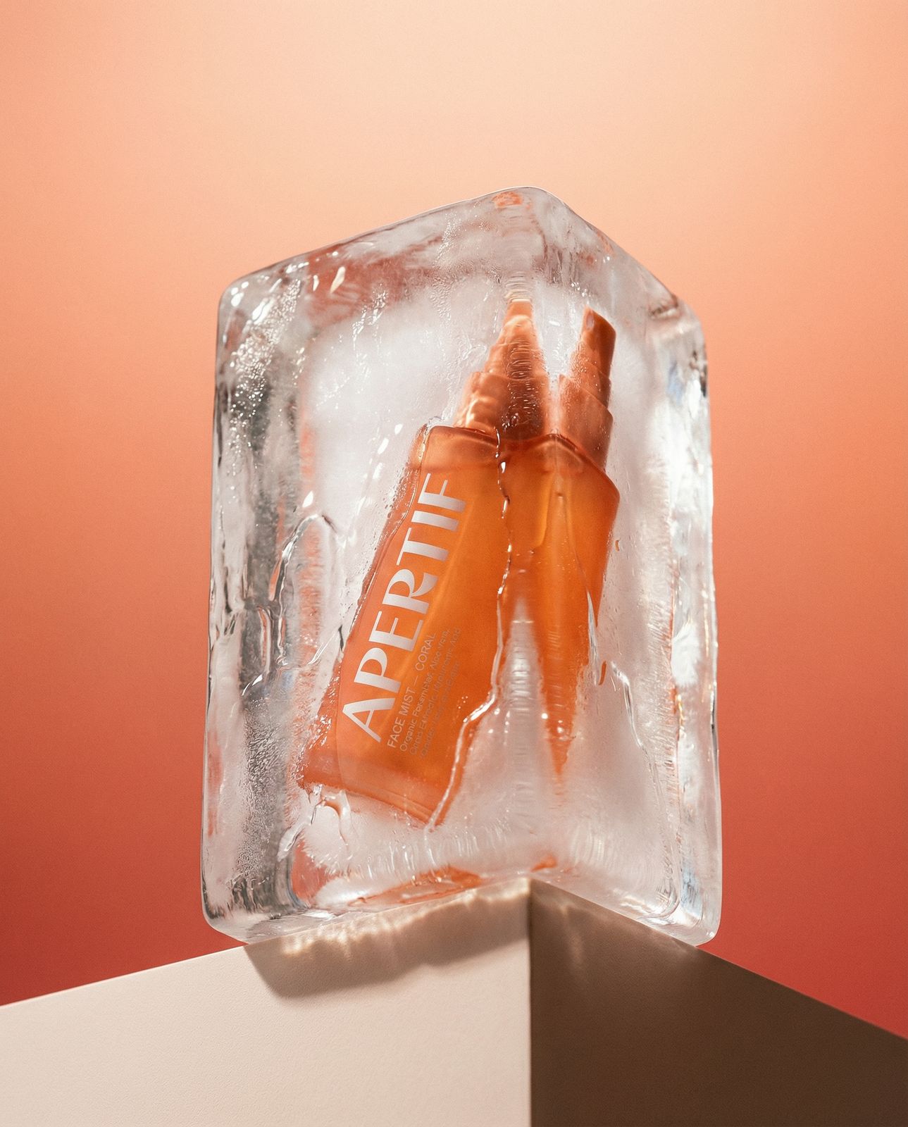an orange beverage in an ice block on a pink background