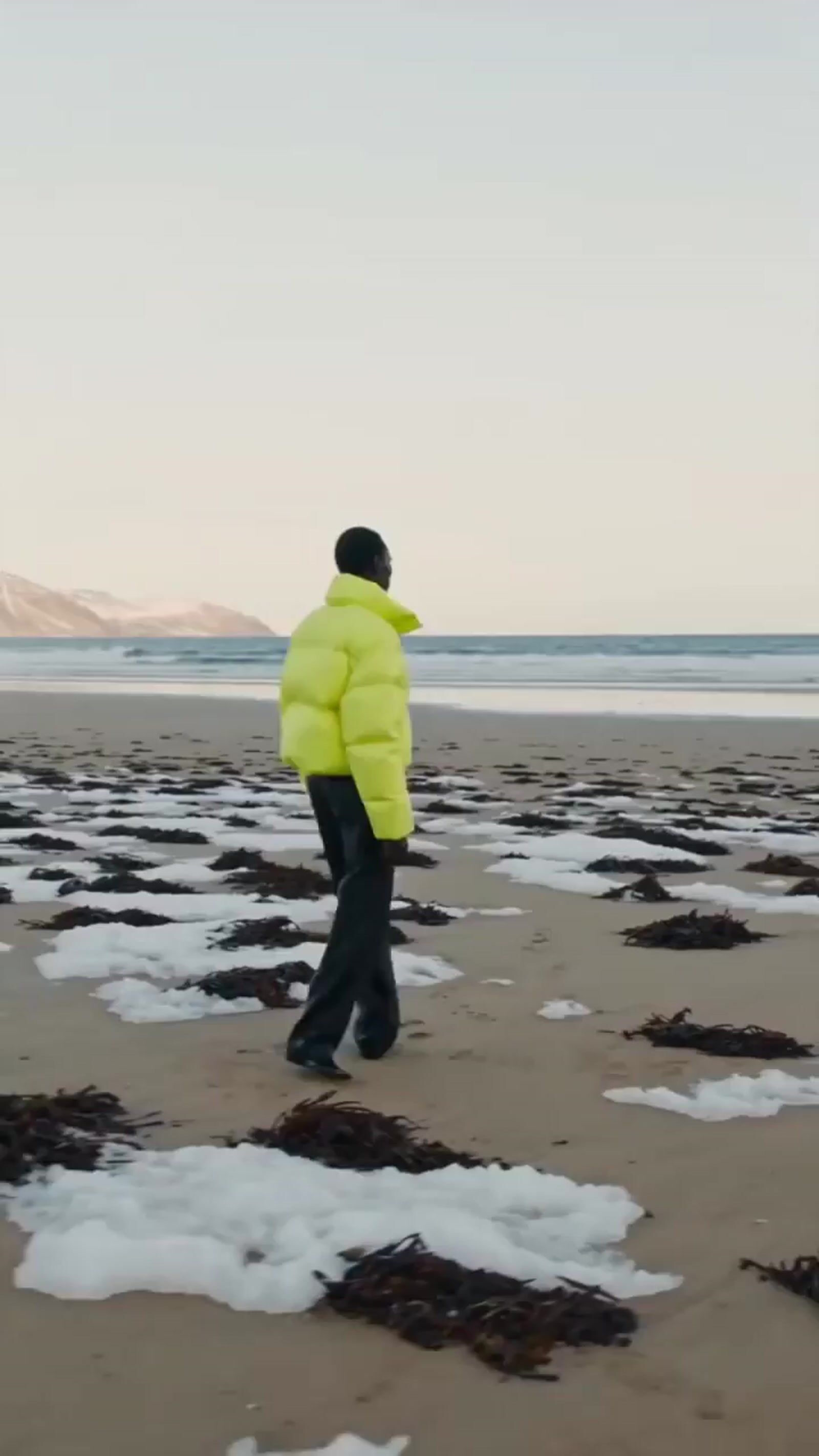 a man in a yellow jacket walking on a beach