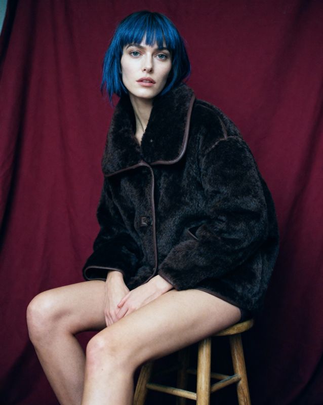 a woman with blue hair sitting on a stool