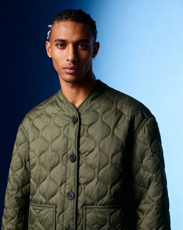 a man in a green jacket standing in front of a blue background